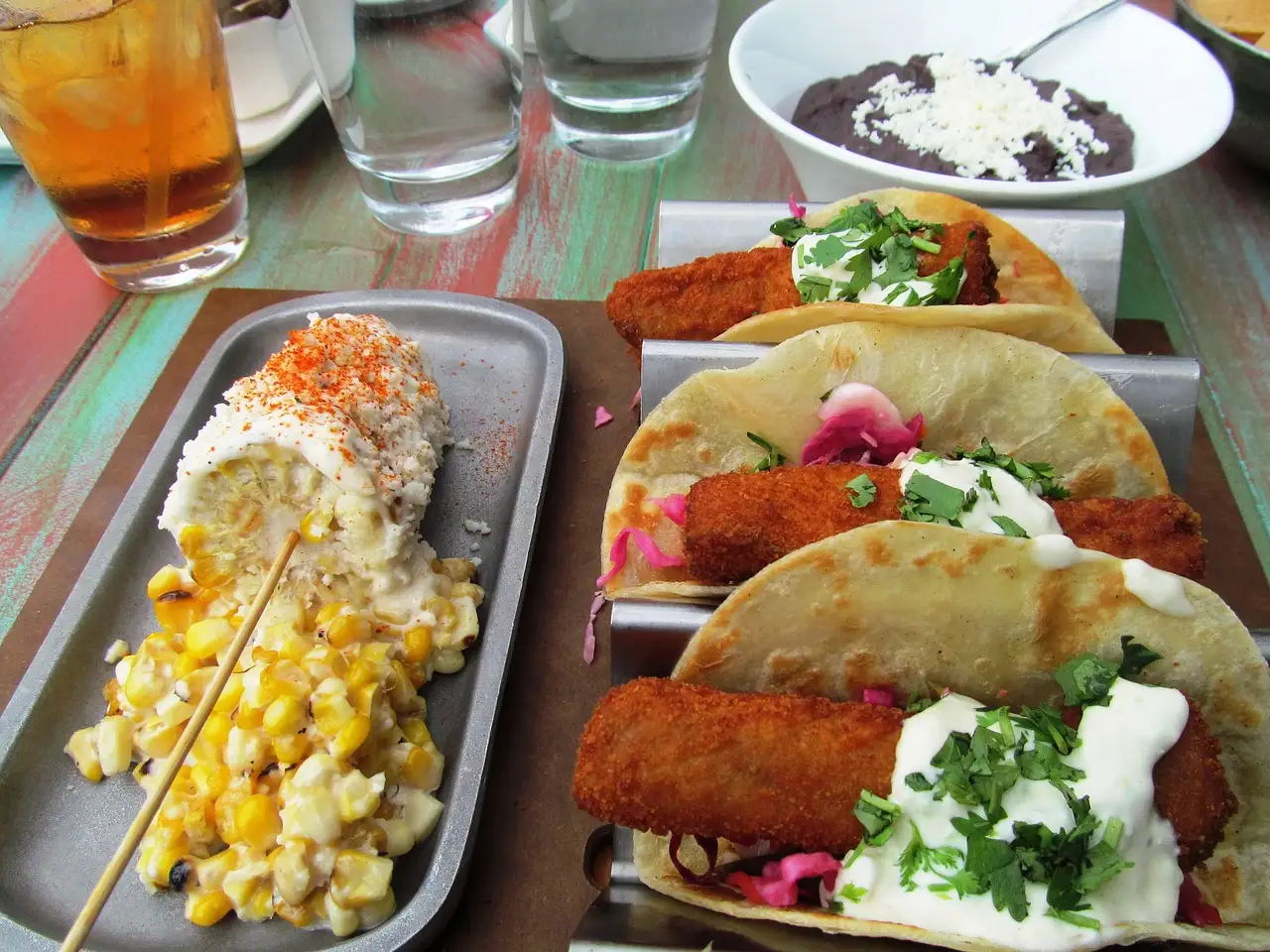 Plate of fish tacos with grilled corn on the cob and drinks on a restaurant table