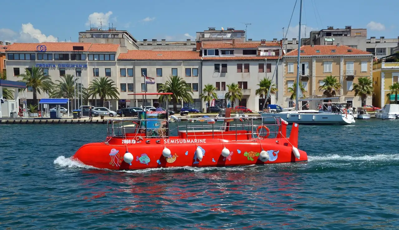 A red glass-bottom tourist boat in a harbor lined with palm trees