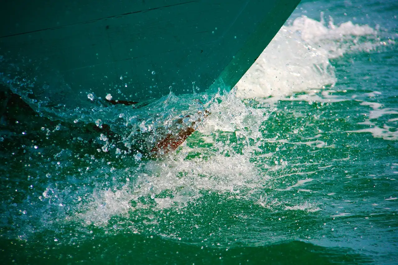 The bow of a boat cutting through green sea water and white spray