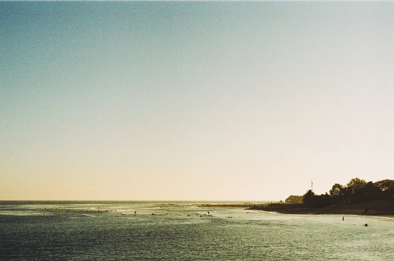 Calm sea off the Malibu coast in hazy evening light, with a wooded point on the horizon