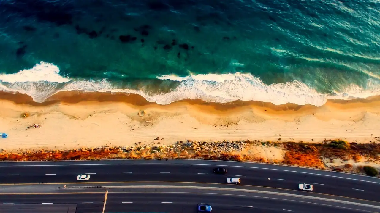 Aerial view of a highway running beside a sandy beach and turquoise surf near Laguna Beach