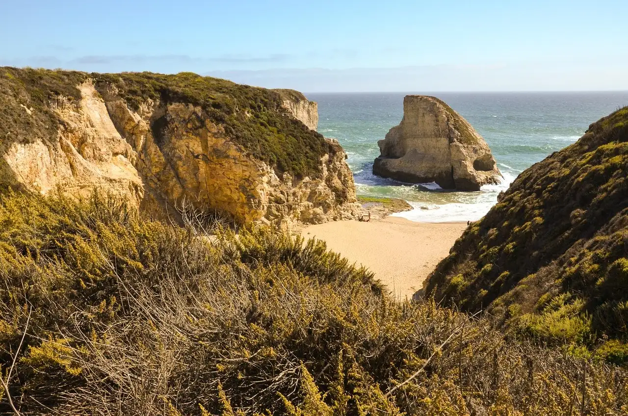 Golden sandstone cliffs and a rock stack above a small sandy cove on the California coast