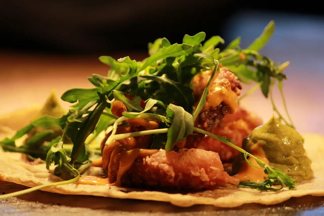 A tortilla topped with fried fish, greens and guacamole