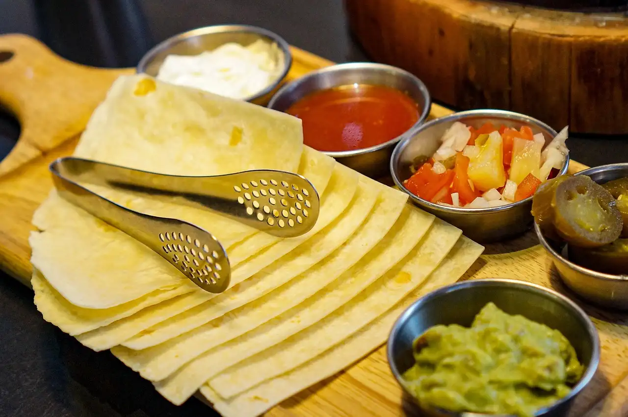 Warm tortillas on a board with bowls of salsa, guacamole and pickled vegetables