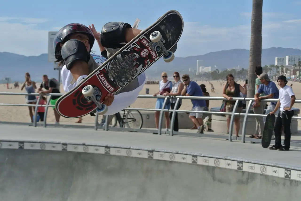 Skateboarder in the air at the Venice Beach skate park with onlookers at the rail