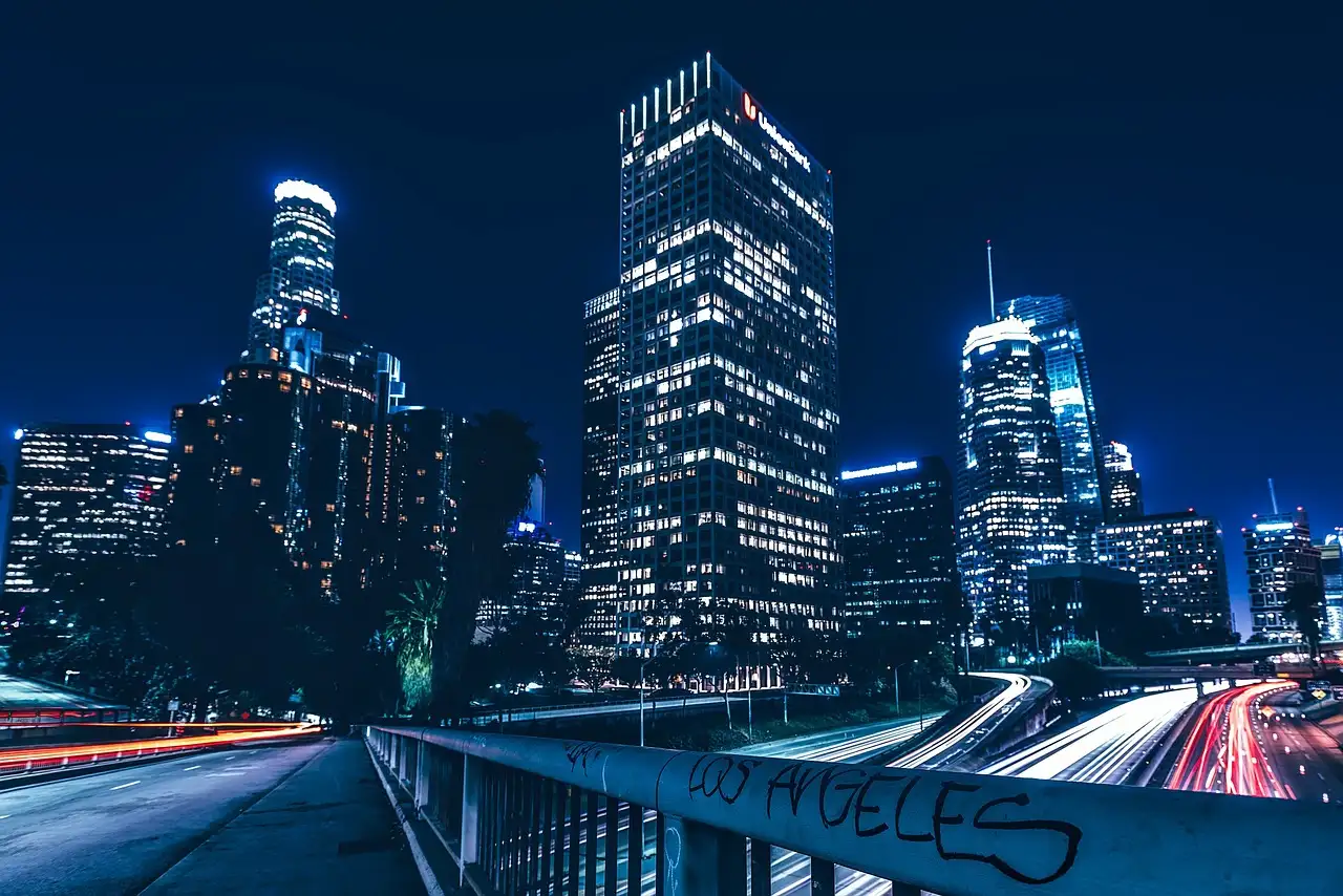 Downtown Los Angeles towers lit up at night above a freeway with light trails