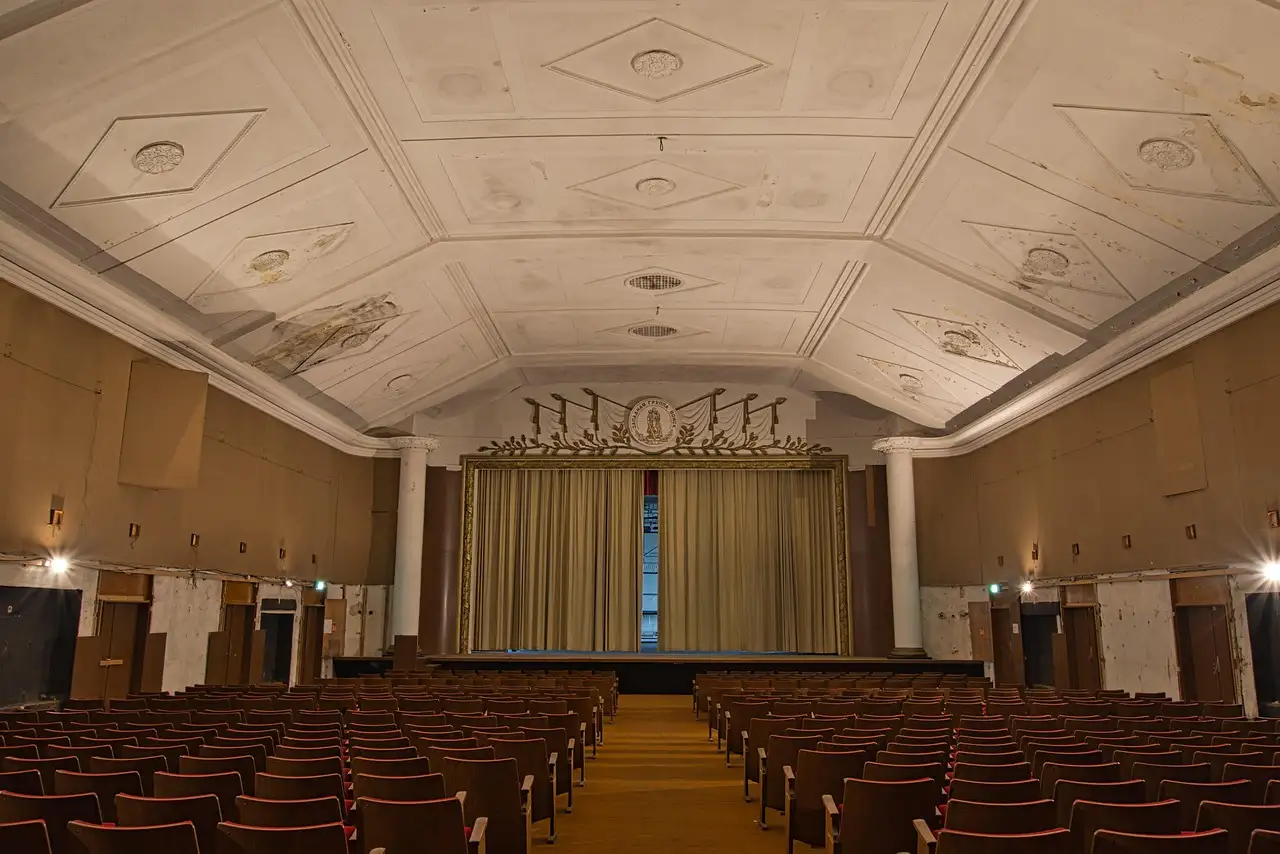 Rows of empty seats facing the curtained stage of an old, deserted theatre