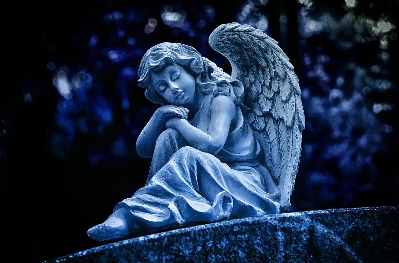 A stone angel statue on a grave, lit in cold blue light