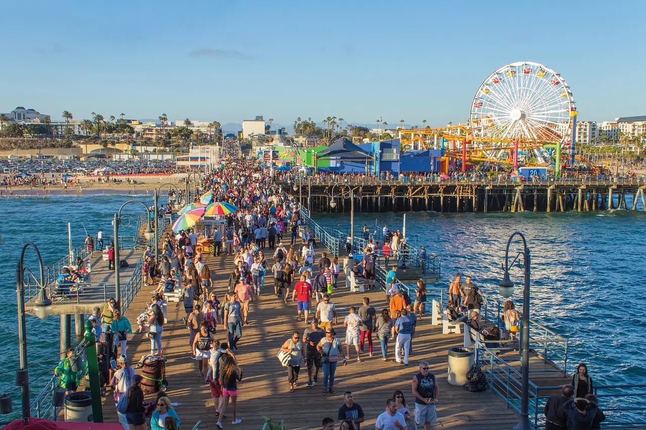 Crowds walking along Santa Monica Pier toward the Ferris wheel on a sunny evening