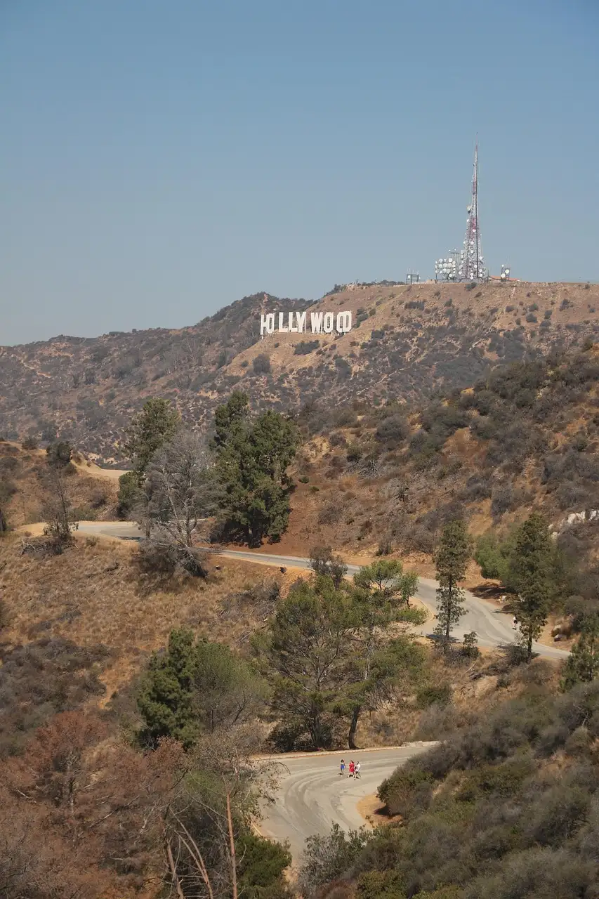 A dirt trail winding through brush in the Hollywood Hills, with the sign far off on the ridge