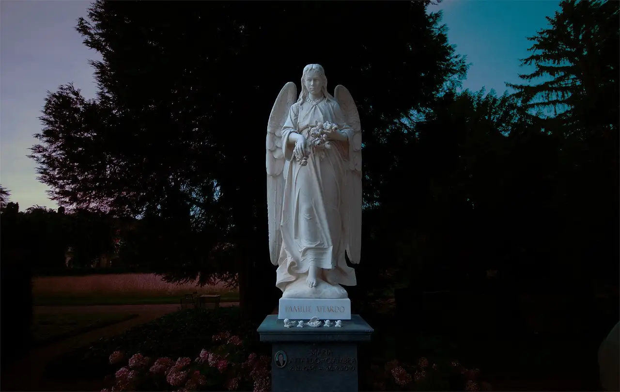 A white angel statue among dark trees at dusk