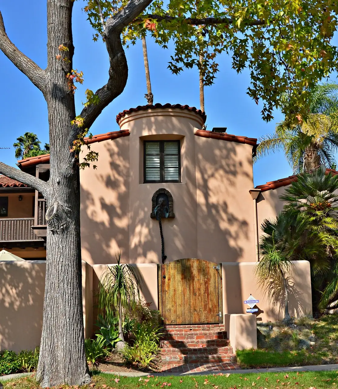 A Spanish-style house with a wooden gate and palm trees on a Beverly Hills street