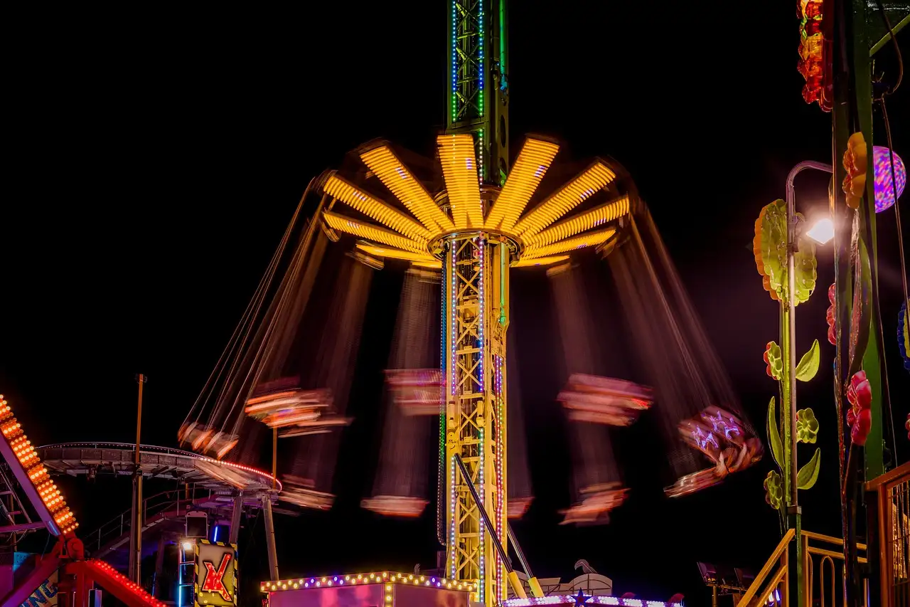 A spinning swing ride lit up in yellow and pink at night in a theme park