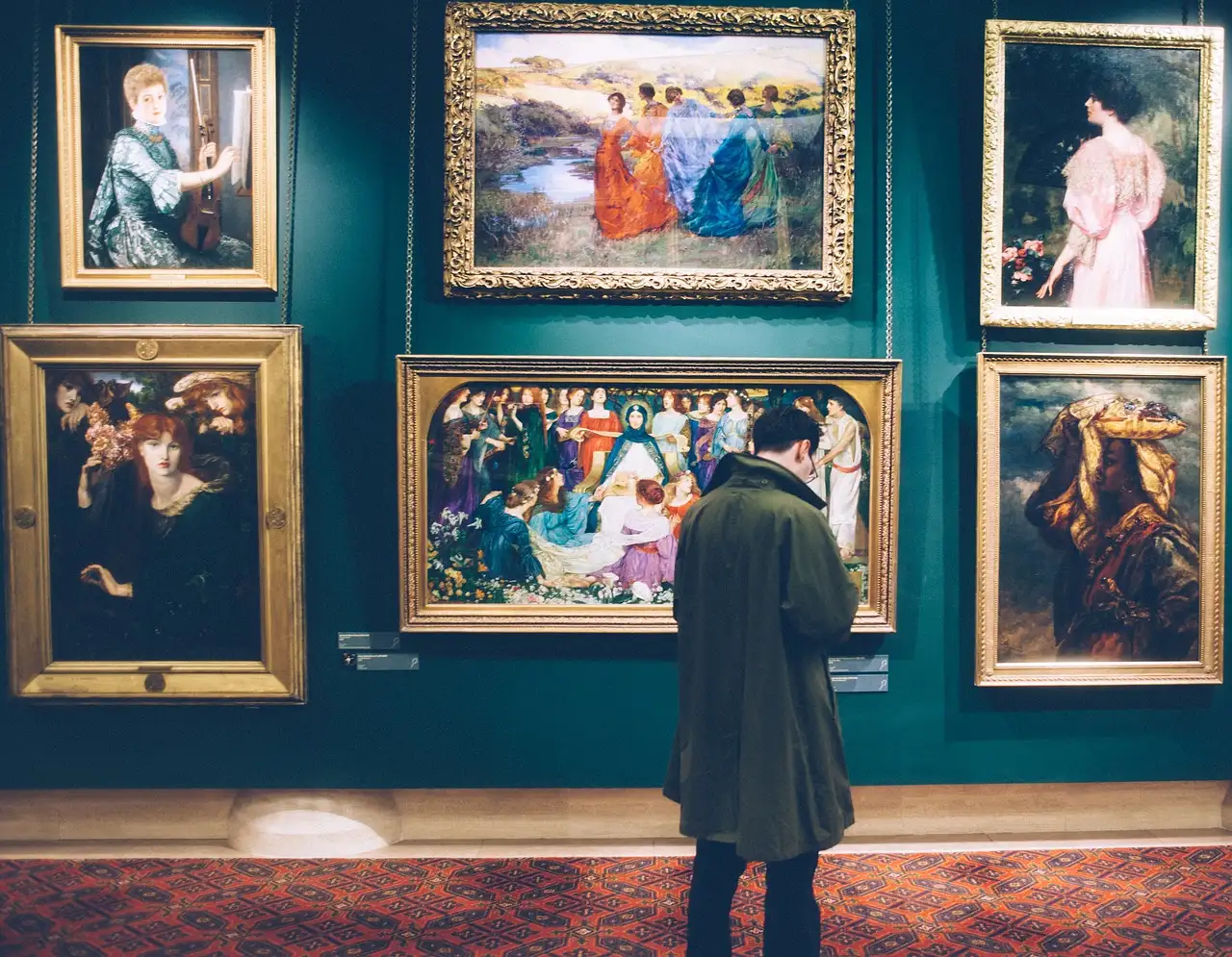 A visitor looking at gold-framed paintings on a dark teal gallery wall