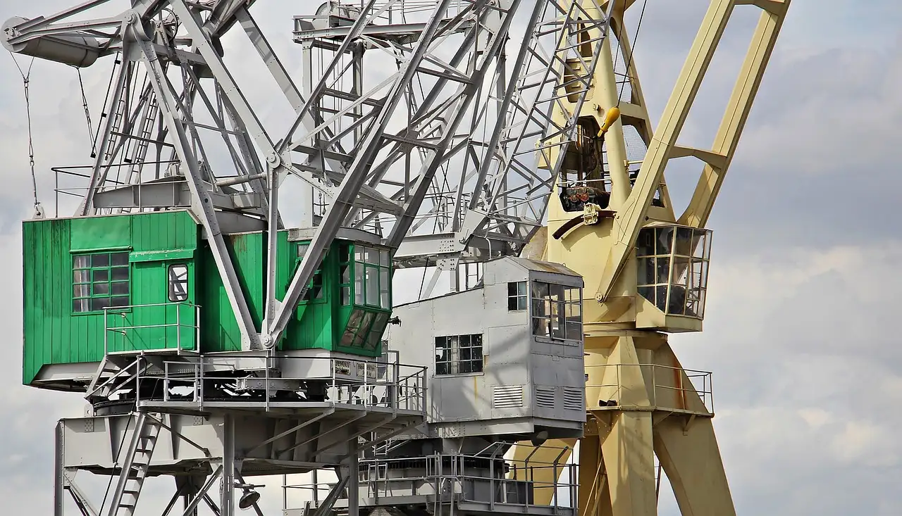 Old green and yellow harbor cranes against a cloudy sky
