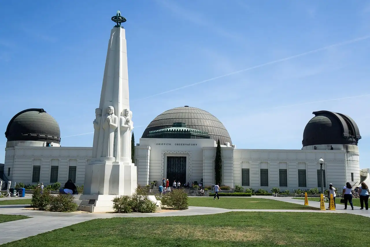 The white Griffith Observatory with its three domes and the Astronomers Monument on the lawn in front