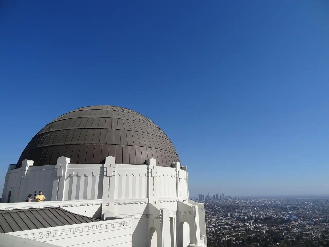 The dome of Griffith Observatory, with the Downtown Los Angeles skyline far off under a blue sky
