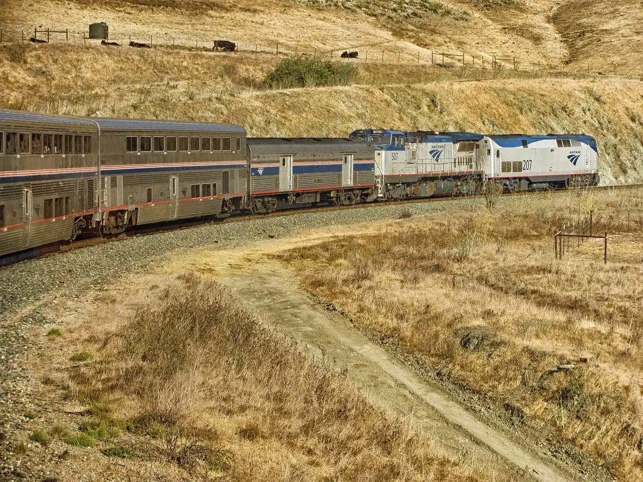 Double-deck Amtrak passenger train curving through dry golden hills in California