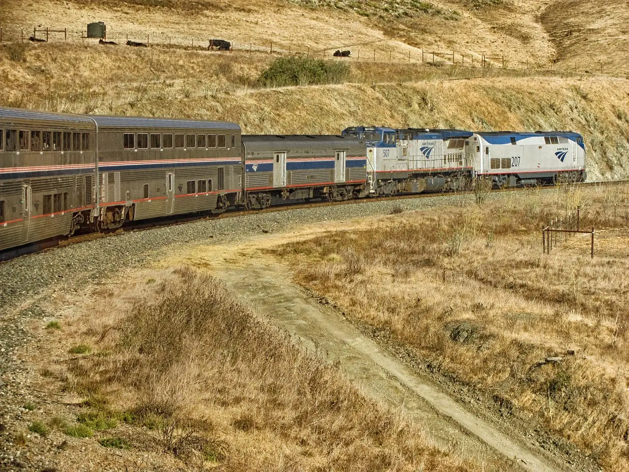 Double-deck Amtrak passenger train curving through dry golden hills in California