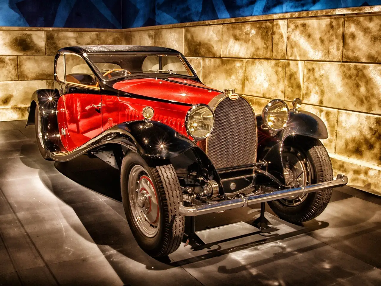 A red and black 1930s sports car on display in a museum hall