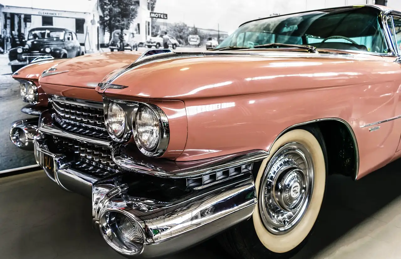 Front of a pink 1950s car with chrome bumpers and whitewall tires in a museum
