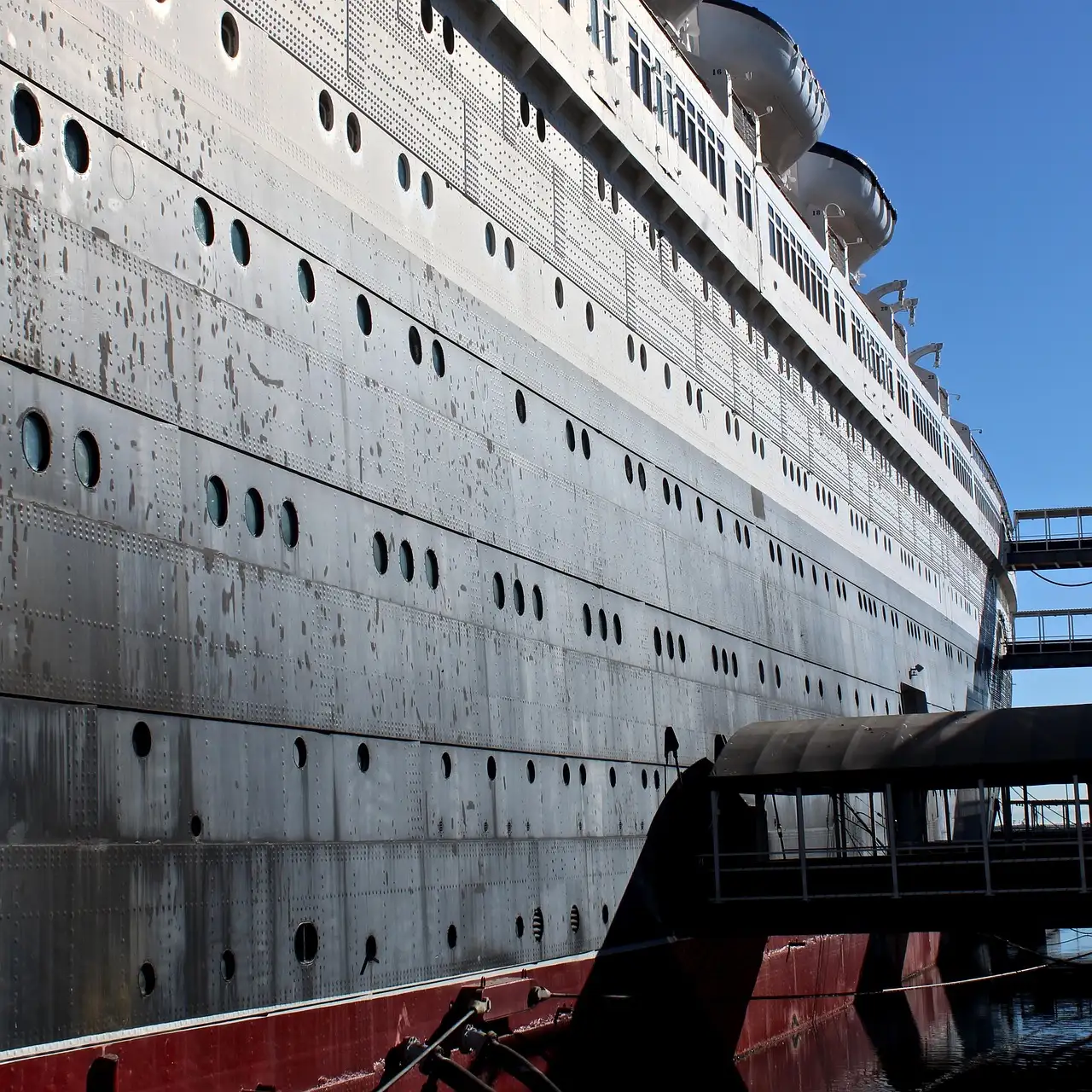 Close view of the Queen Mary's riveted grey hull with rows of round portholes and lifeboats above