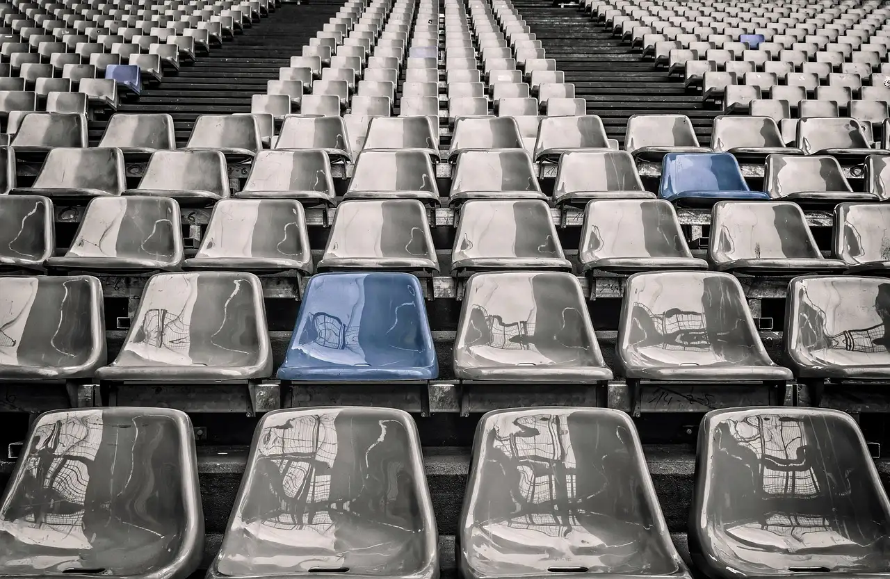 Rows of empty grey stadium seats with a few blue seats among them