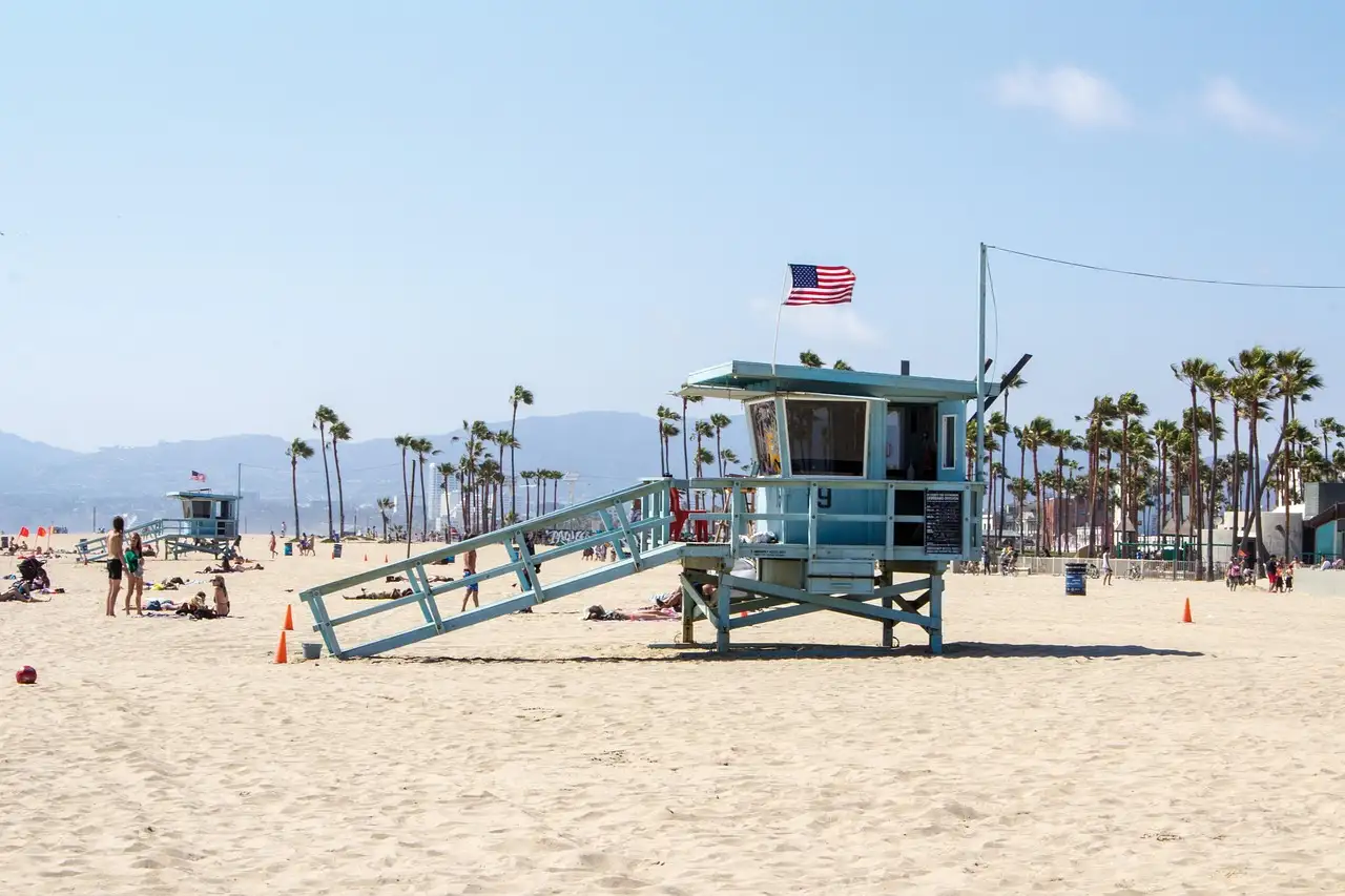 A blue lifeguard tower with a US flag on a wide sunny beach lined with palms