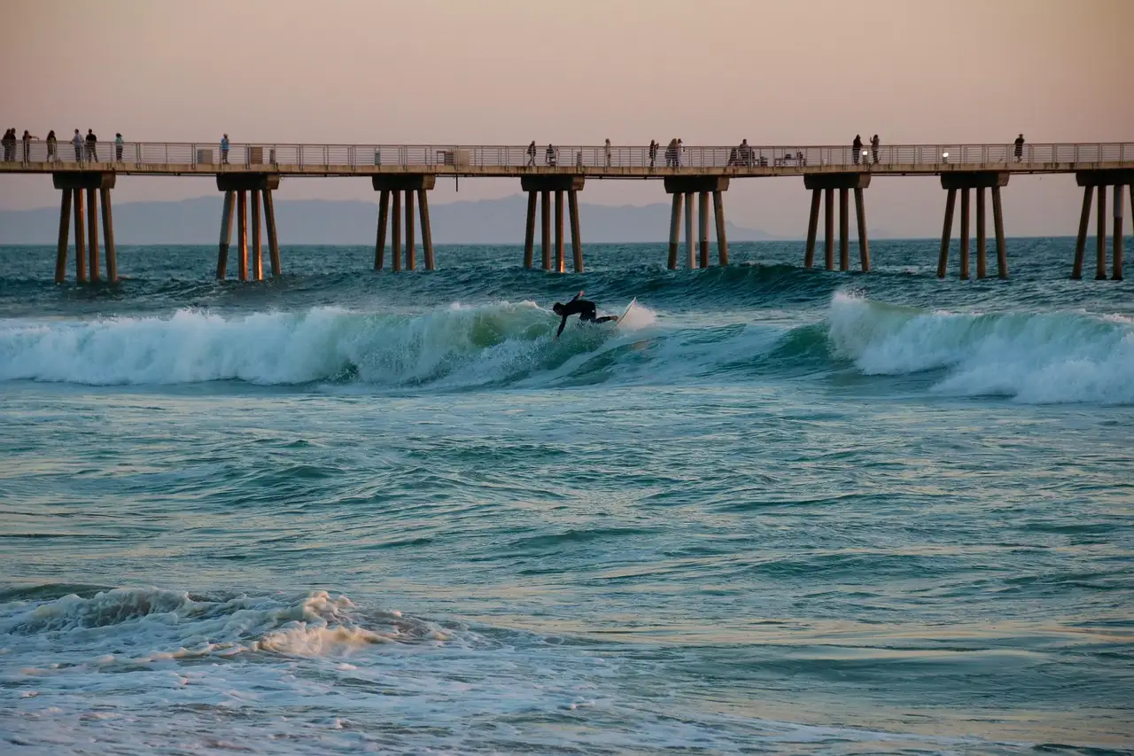 Surfer riding a wave beside Hermosa Beach pier, the next town south of Manhattan Beach