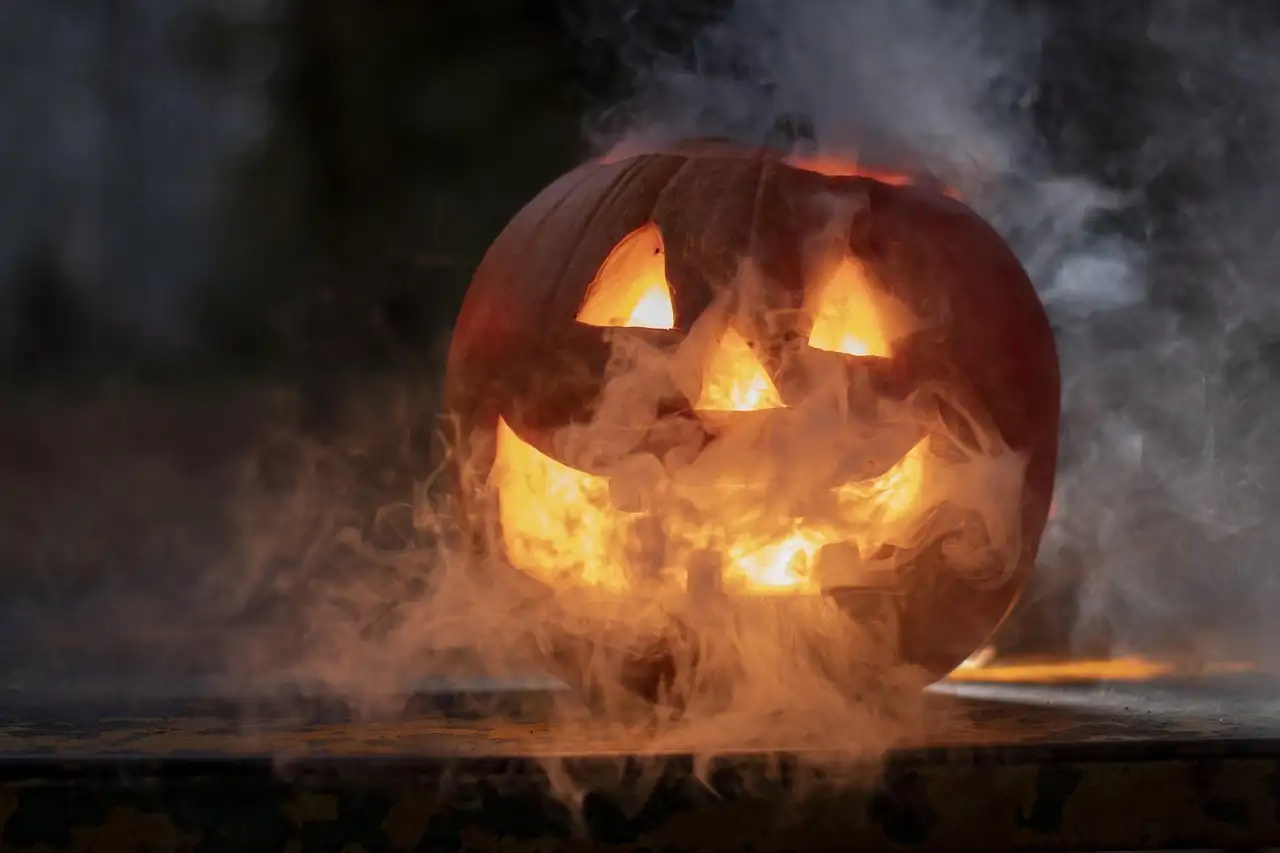 A carved pumpkin lantern glowing in the dark with smoke around it