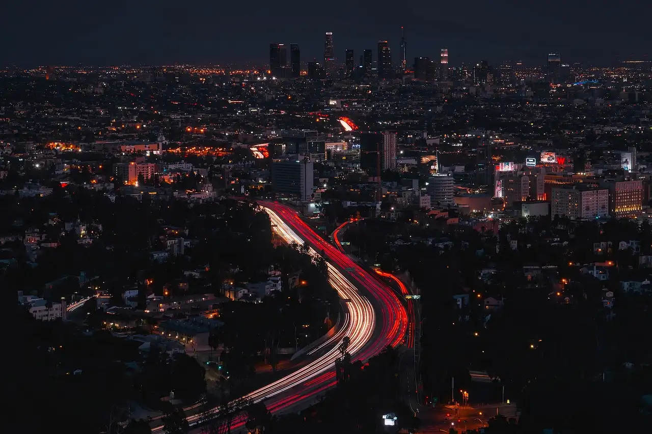 Light trails on a curving freeway at night, with the Downtown Los Angeles towers far behind