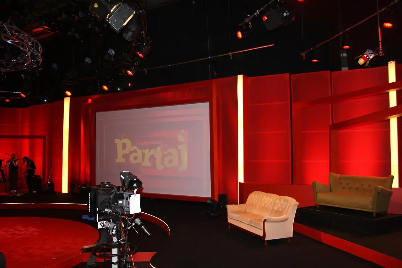 A TV studio set with a studio camera, red walls, stage lights and two sofas